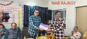 A man in a plaid shirt (likely a dignitary or guest of honor) is seen presenting a certificate to a visually impaired man wearing glasses and a similar patterned shirt. Both individuals are smiling, conveying a moment of pride and accomplishment.