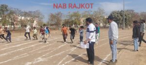 A group of visually impaired athletes are sprinting on a marked dirt track, wearing blindfolds or using guides—highlighting an inclusive, accessible sporting event. One boy and several organizers on the right are seen monitoring the race with clipboards and notes, adding structure and supervision.