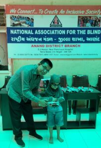 This image captures a distribution event organized by the National Association for the Blind (NAB), Anand District Branch, aimed at supporting visually impaired children.